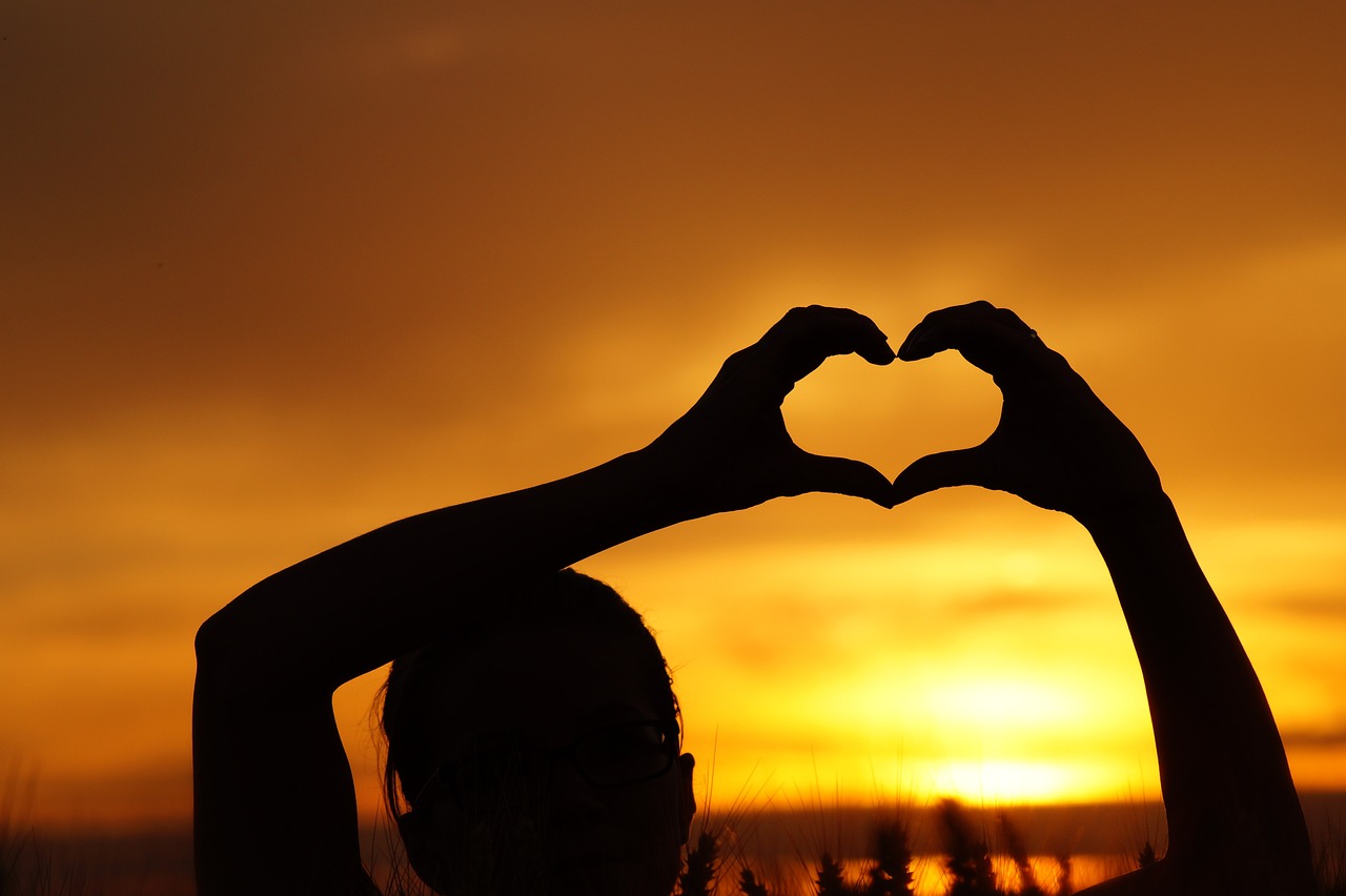 Sunset silhouette of two hands forming a heart, symbolizing love, family, and emotional growth