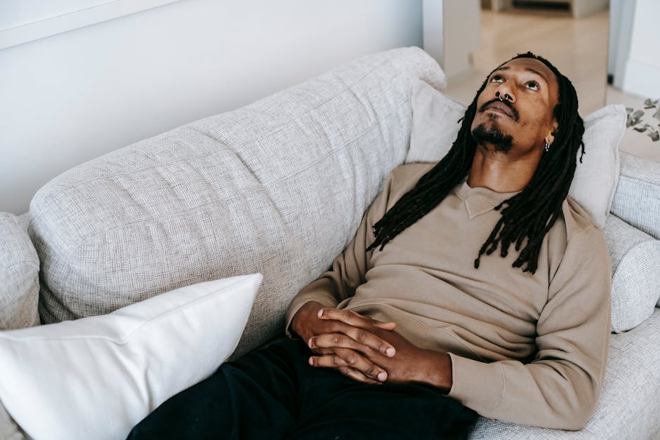 Man with dreadlocks lies on a couch, looking introspective and reflecting, symbolizing recovery and emotional healing.